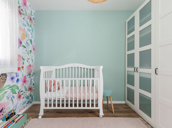 עיצוב עדין לחדר תינוקת- טפט פרחוני, קירות בגוון ירוק מרווה, רהיטים לבנים ושטיח ורדרד.