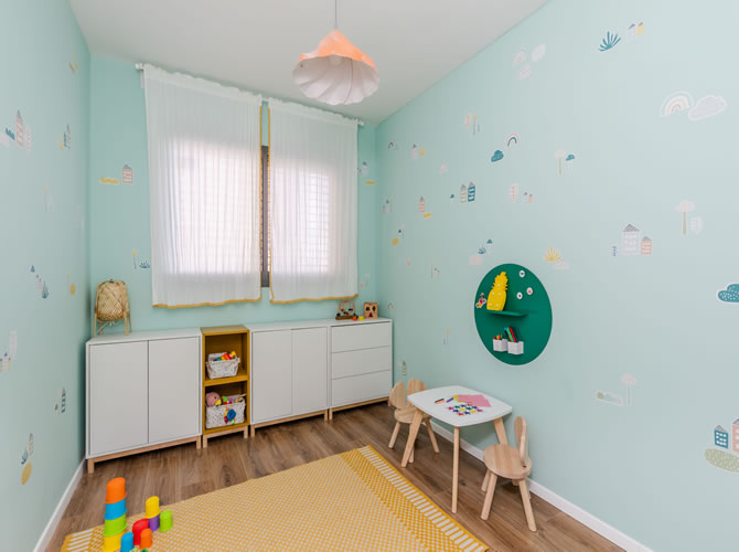 חדר משחקים עם ארונית משחקים מאיקאה, קירות בגוון ירוק אקווה עם מדבקות ושטיח צהוב.