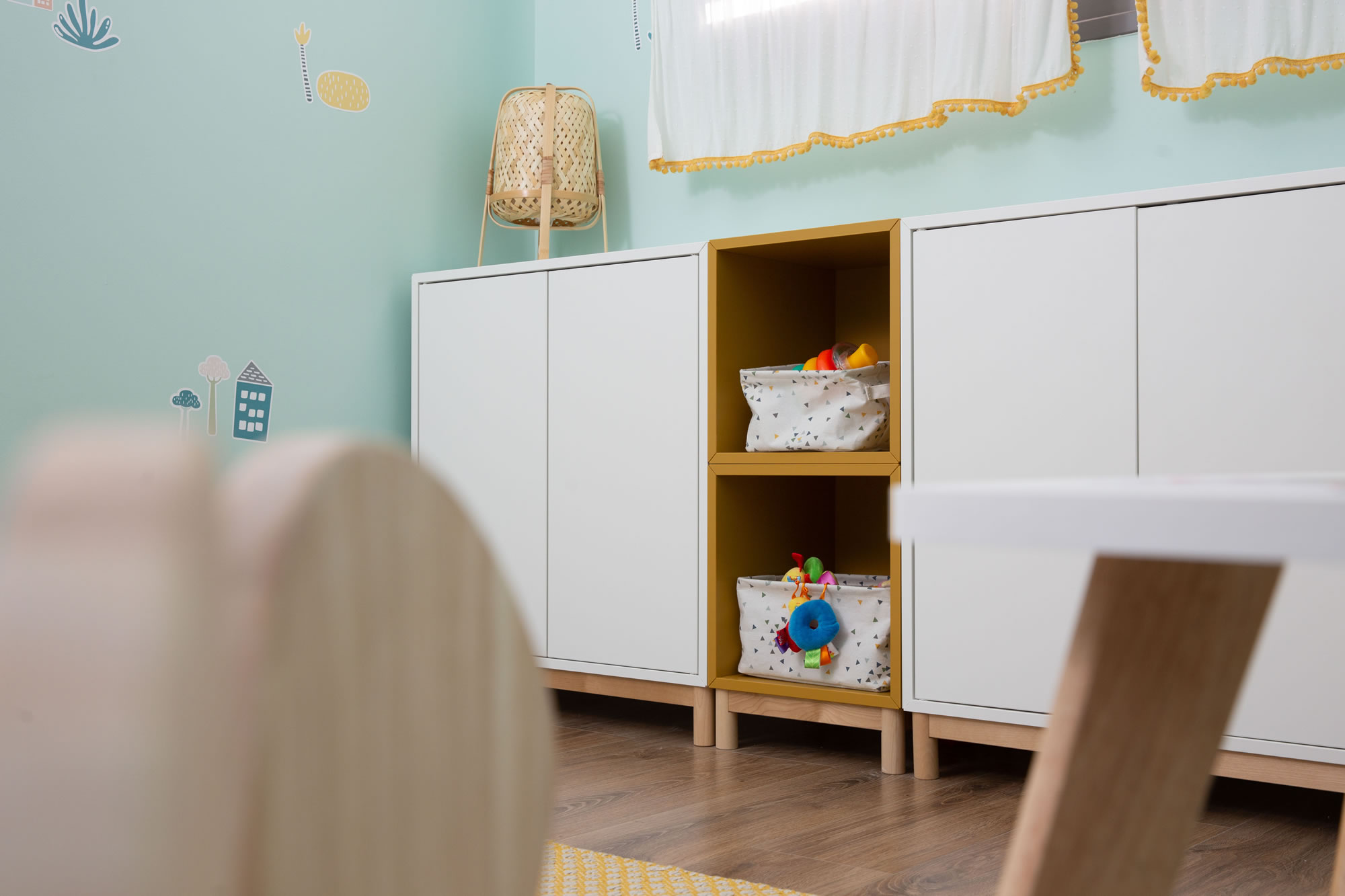 ארוניות מאיקאה בגווני לבן וצהוב ורגלי עץ משתלבות בדיוק עם הוילון, הפרקט והשטיח בחדר המשחקים.