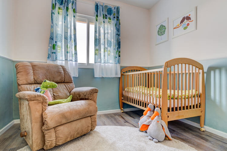 חדר תינוק בצבעוניות רגועה עם קרניז דקורטיבי על הקירות. 