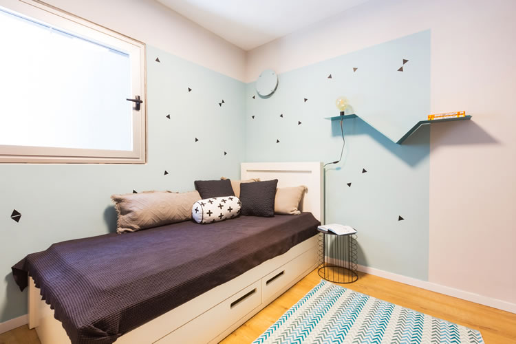 עיצוב חדר שינה לנער, איזור המיטה תחום בצבע קיר בגוון אקווה עם מדבקות משולשים.
